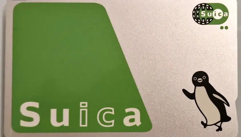 Eine Suica-Karte mit einem fröhlichen Pinguin-Motiv. Die Karte ist silberfarben mit einem großen grünen Feld und dem Schriftzug "Suica".