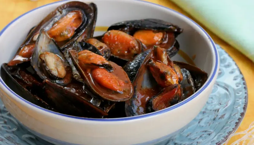 Un invitante sautè di cozze, succulente e profumate, servite in una ciotola bianca con bordo blu.