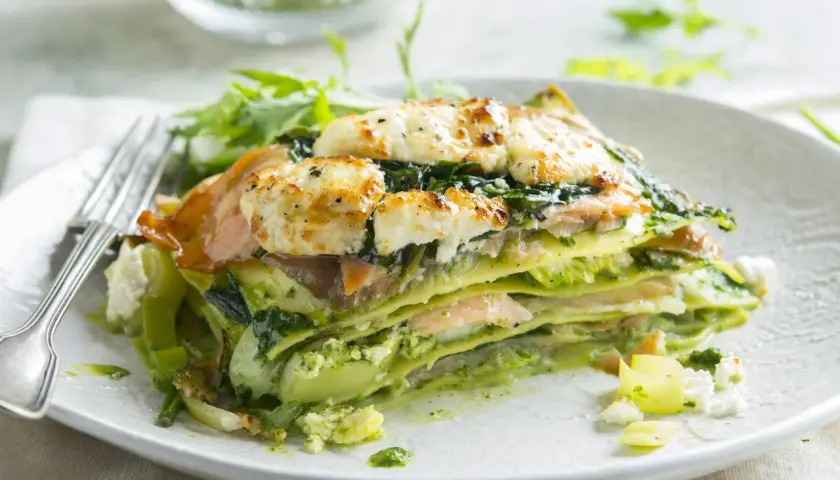 Une part de lasagne saumon épinard, gratinée au fromage, servie avec une salade verte.