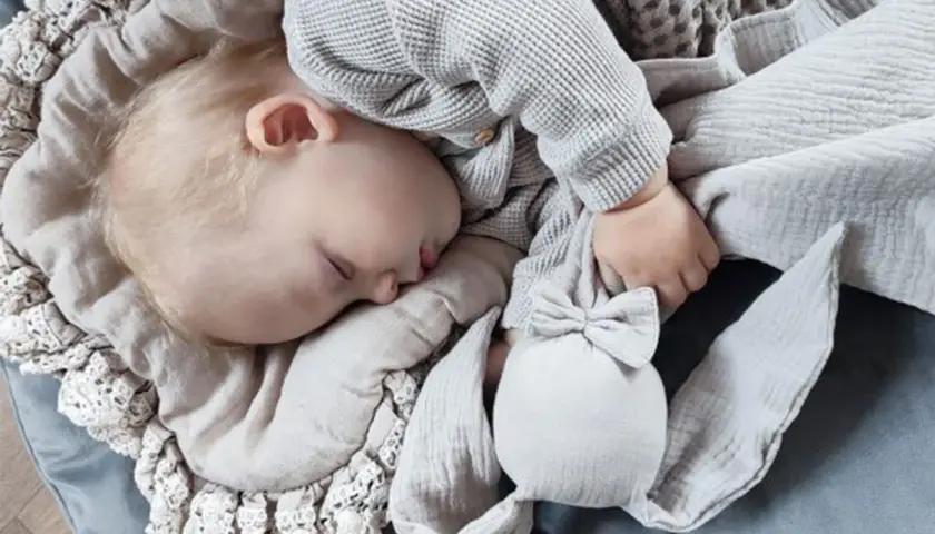 Śpiące dziecko wtulone w miękką kocyk, obok niego króliczek – idealna pierwsza przytulanka dla noworodka.