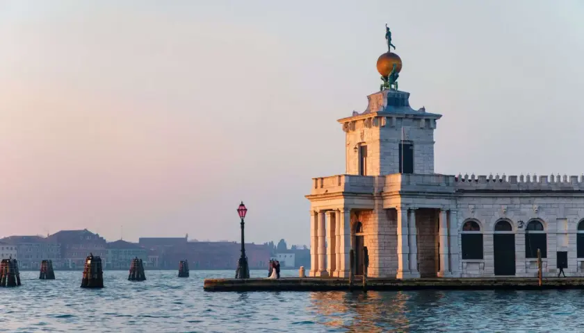 La Dogana di Venezia, un bâtiment historique, se dresse au bord de l'eau. Un couple s'embrasse près d'un lampadaire.