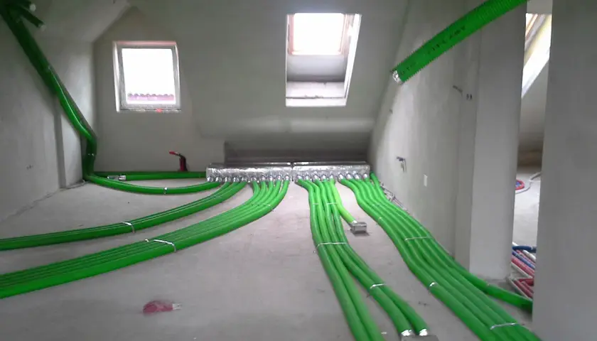 Instalacja rekuperacji w podłodze: zielone rury wentylacyjne rozchodzą się po pomieszczeniu, tworząc skomplikowaną sieć.