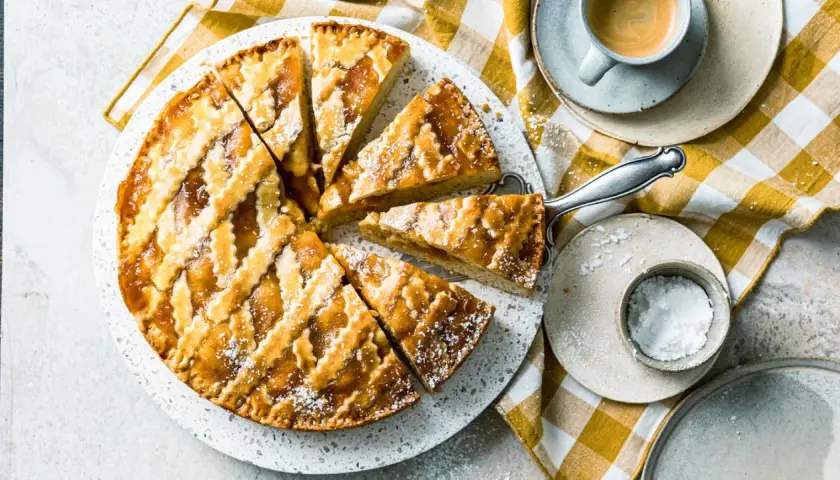Ein köstliches Crostata-Rezept, aufgeschnitten und mit Puderzucker bestäubt, daneben eine Tasse Espresso.