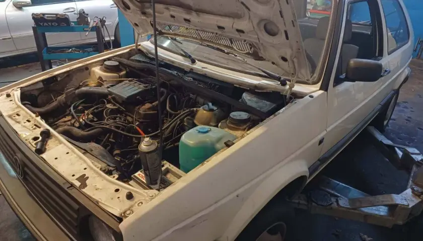 Biały Volkswagen Golf z otwartą maską, silnik gotowy do wyjęcia. Zastanawiasz się, ile kosztuje wyciągnięcie silnika?