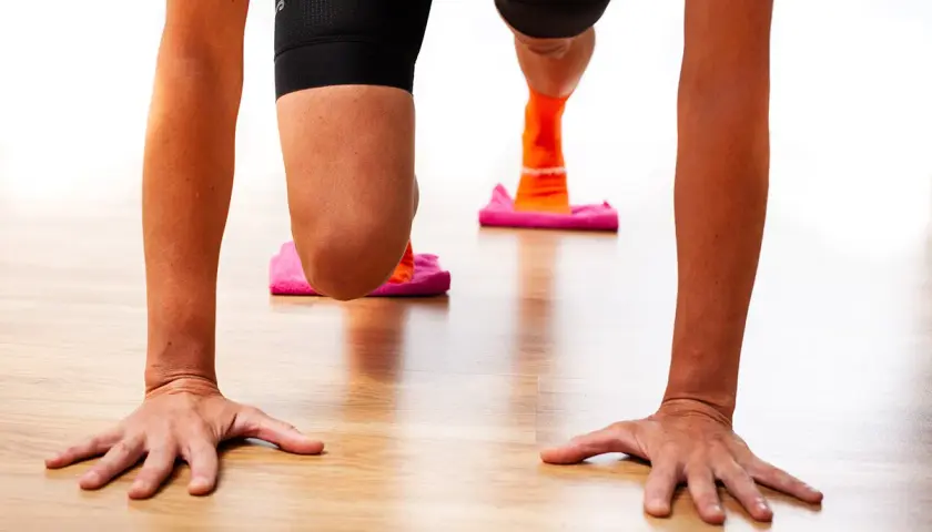 Manos en el suelo, rodillas flexionadas sobre discos deslizantes. Ejercicio para fortalecer rodilla.