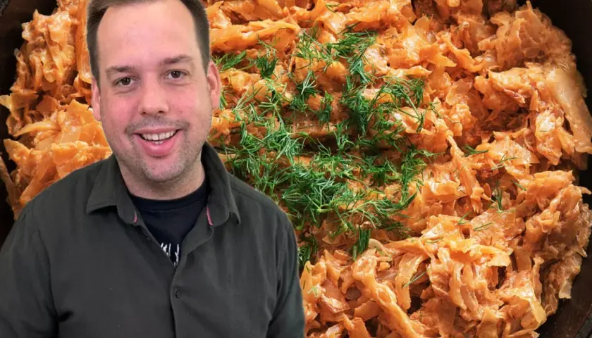 Uśmiechnięty mężczyzna obok patelni z pyszną, babciną kapustą zasmażaną, ozdobioną świeżym koperkiem.
