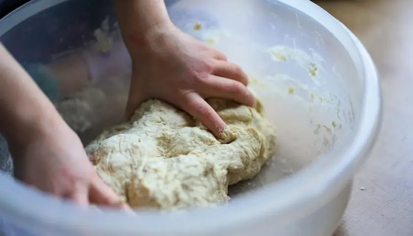 Dziecko zagniata ciasto w misce. Czy weganie jedzą drożdże? Tak, drożdże to grzyby, więc są wegańskie.