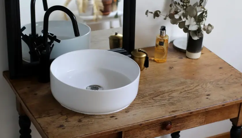 Un plan pour créer son meuble de salle de bain : vasque blanche, robinetterie noire, miroir et accessoires déco sur un meuble ancien.