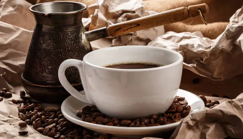 Ein traditioneller Mokkakanne und eine Tasse mit griechischem Mokka, umgeben von Kaffeebohnen und zerknülltem Papier.