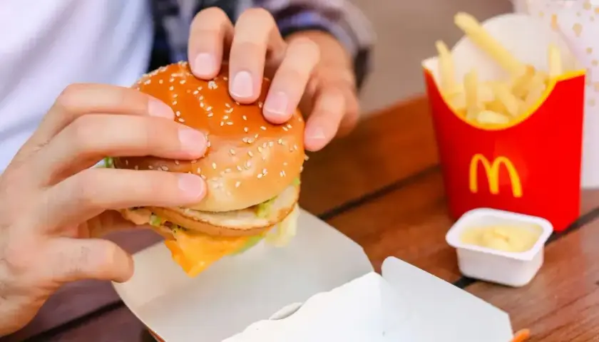 Ręce trzymają burgera z McDonald's, obok frytki i sos śmietanowy z mąką.