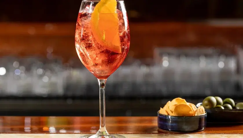Un bicchiere di Aperol Spritz, rinfrescante e colorato, pronto per un aperitivo con patatine e olive.