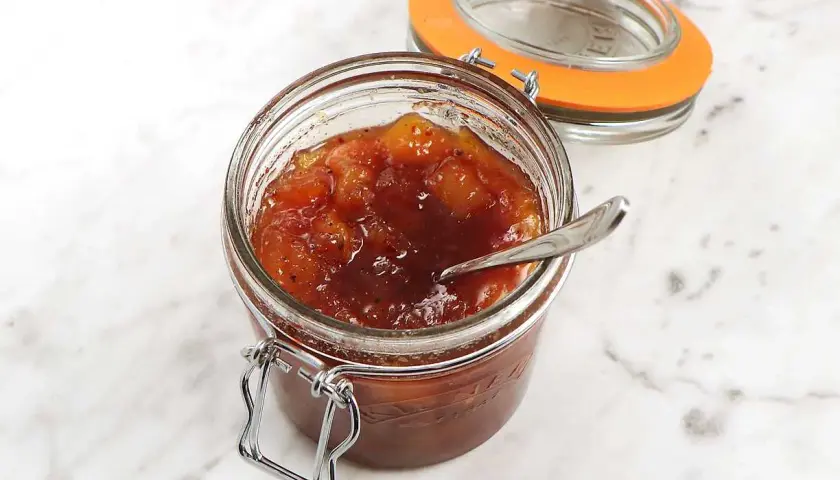 En burk med hemlagad mango chutney, perfekt för ditt nästa mango chutney recept. En sked vilar i den söta, kryddiga blandningen.