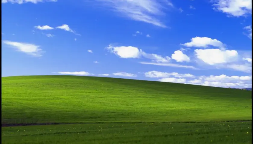 Zielone wzgórze pod błękitnym niebem z chmurami, ikoniczny widok z **win xp virtual machine**.