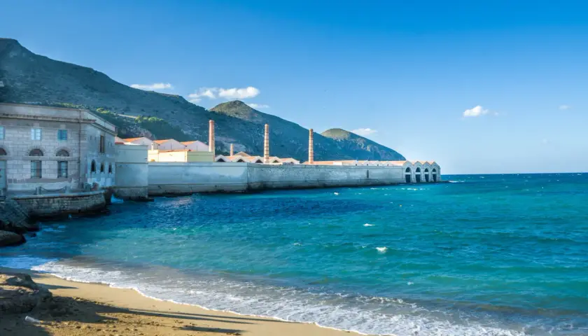 Ancienne conserverie de thon à Favignana, Sicile, avec ses cheminées emblématiques se dressant face à la mer turquoise.