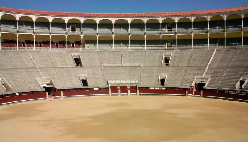 Vista interior de una plaza de toros vacía, con gradas de piedra y balcones arqueados. Las ventas por dentro esperan al público.