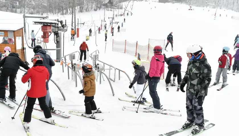 Ludzie w strojach narciarskich stoją w kolejce do wyciągu narciarskiego na ośnieżonym stoku.