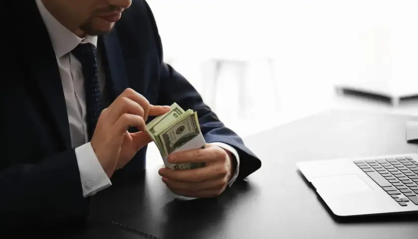 Mężczyzna w garniturze liczy banknoty dolarowe przy biurku. Jego praca w banku wymaga precyzji.