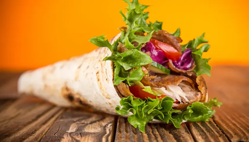 Kebab zawinięty w placek z mięsem, warzywami i sałatą na drewnianym stole.