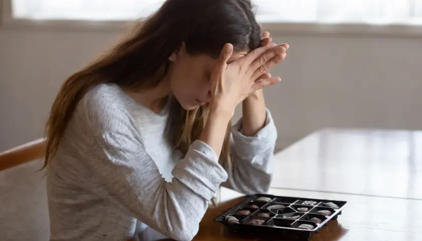 Donna con le mani sul viso, davanti a una scatola di cioccolatini, forse cercando un antidepressivo naturale più potente.
