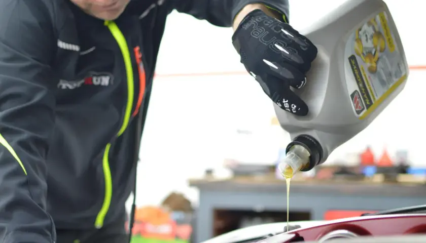 Mechanik w rękawiczkach nalewa olej do silnika. Dowiedz się, ile kosztuje wymiana oleju i filtrów u mechanika.