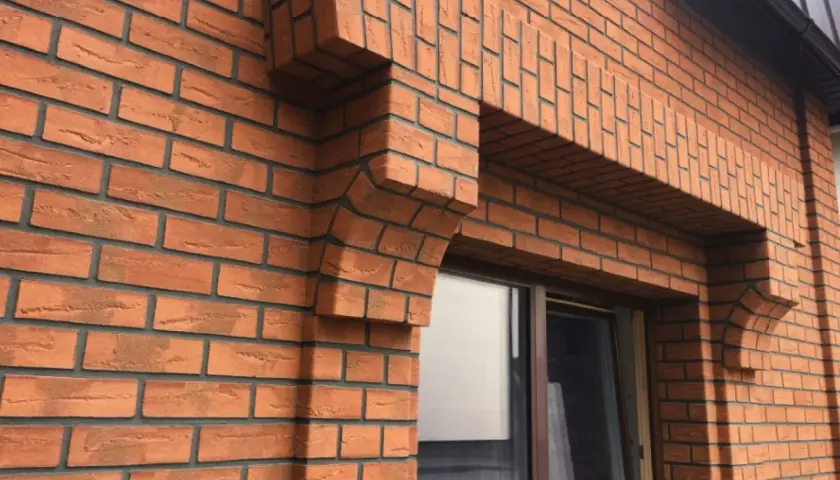 Fragment elewacji z cegły klinkierowej z ozdobnym gzymsem nad oknem.