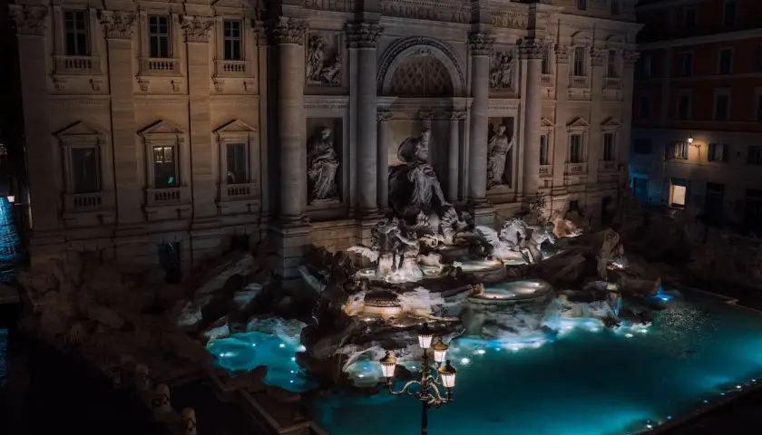 Fontana di Trevi a Roma di notte, con le sue sculture illuminate e l'acqua turchese che brilla sotto i lampioni.