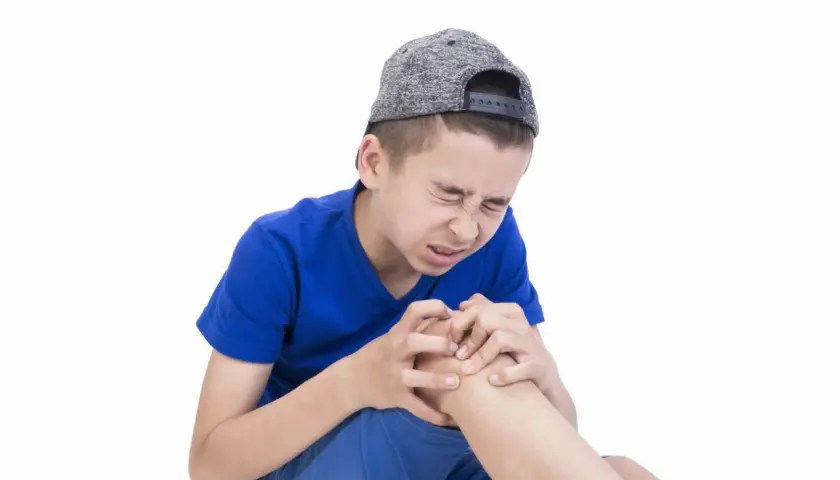 Ragazzo con cappellino grigio stringe il ginocchio con espressione sofferente, forse a causa dei dolori della crescita.