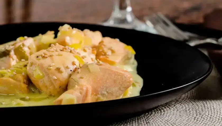 Délicieuse blanquette de saumon au vin blanc, parsemée de graines de sésame, servie dans une assiette noire.