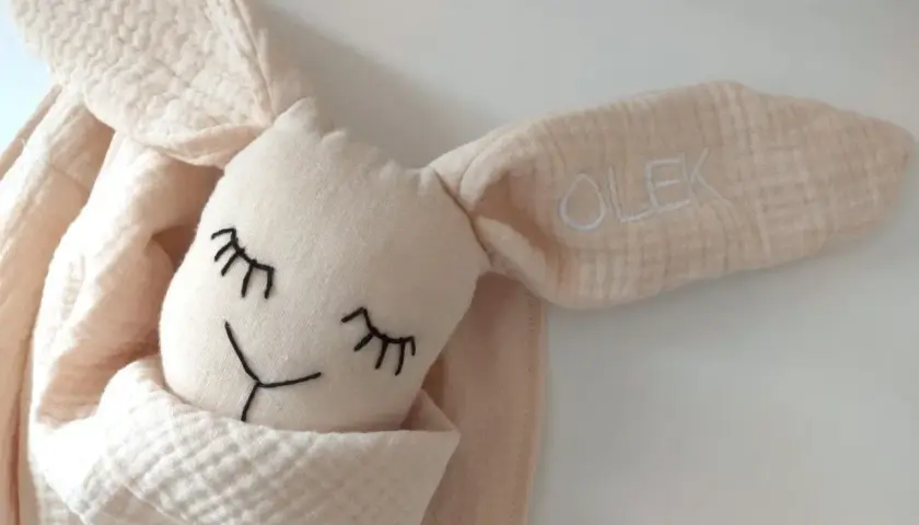 Urocza, beżowa przytulanka dla noworodka z haftowanym imieniem "OLEK" na uszku. Idealna pierwsza przytulanka.