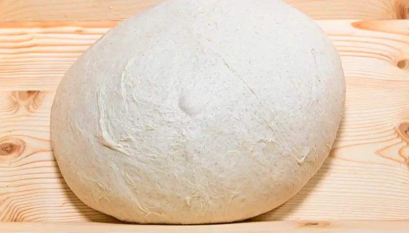 Impasto lievitato per pizza in casa, pronto per essere steso su un tagliere di legno.
