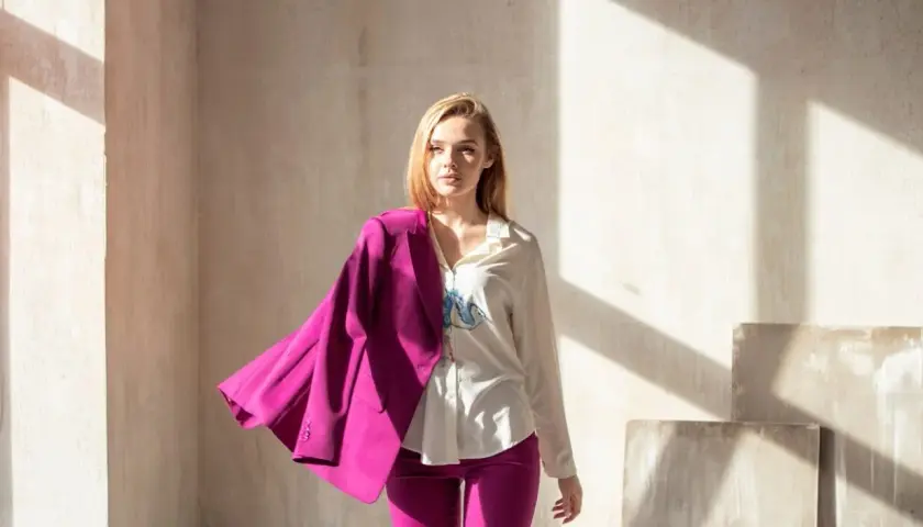 Młoda kobieta w eleganckim garniturze w intensywnym, **magenta kolorze**. Marynarka narzucona na ramię, spodnie podkreślają sylwetkę.