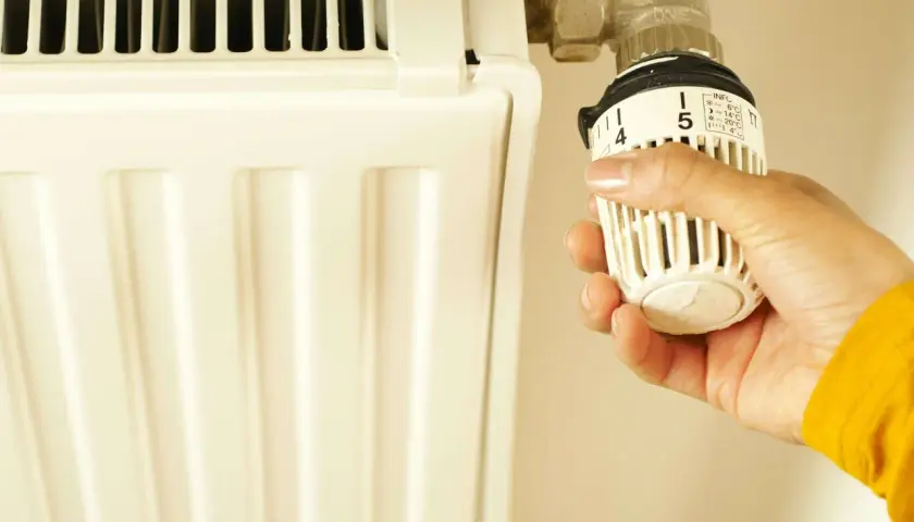 Mano ajustando el termostato de la calefacción para ahorrar. Aprende como regular el termostato de la calefacción para ahorrar energía y dinero.