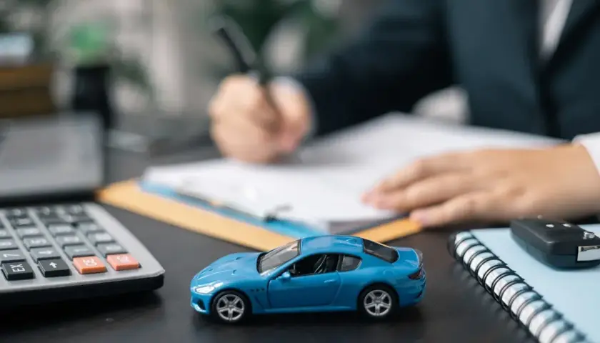 Niebieski model samochodu, kalkulator i kluczyki na biurku. Dłoń pisze na umowie, sugerując honda leasing.