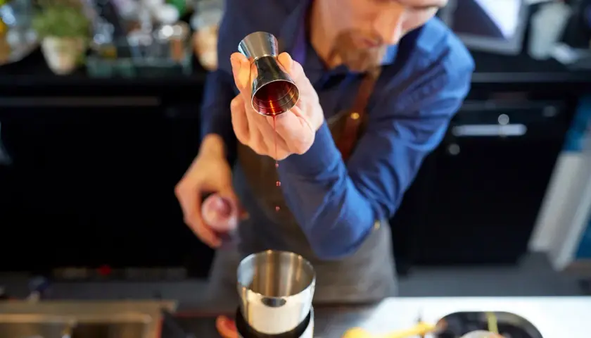 Barman przelewa czerwony płyn z jiggera do shakera.