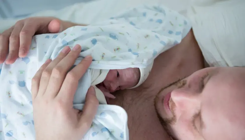Ciepłe kangurowanie przez tatę po cesarce. Maluszek wtulony w klatkę piersiową ojca, czuje jego bicie serca.