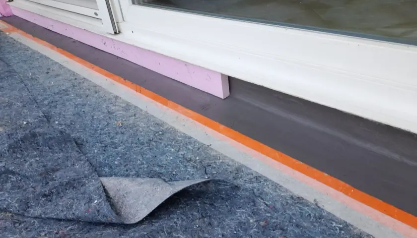 Schutzmatte liegt bereit, um den Sockel abzudichten. Dämmung und Abdichtung am Fenster sind sichtbar.
