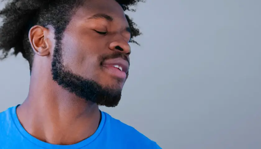 Hombre con ojos cerrados y barba cuidada, parece disfrutar de un momento de paz. Sus perillas resaltan su rostro.