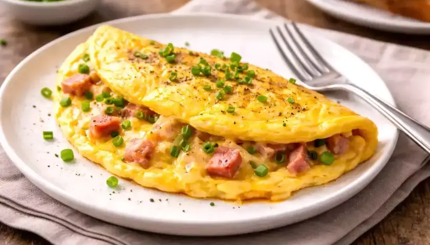 Une omelette simple et dorée, garnie de dés de jambon et de ciboule fraîche, prête à être dégustée.