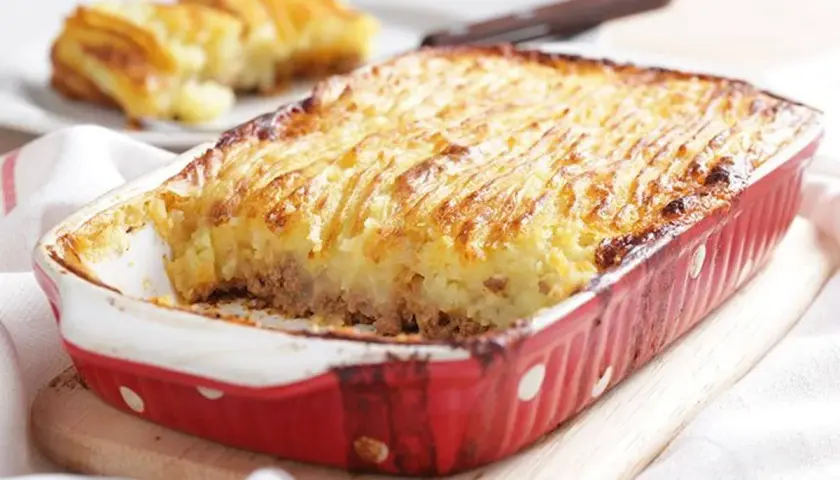 Un plat de hachis parmentier, dont l'origine remonte à Antoine-Augustin Parmentier, est servi dans un plat rouge à pois blancs.