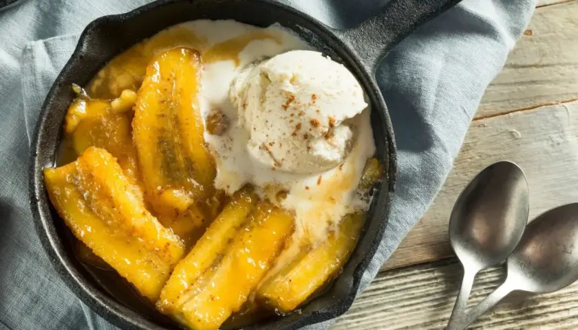Banane flambée servie dans une poêle en fonte, nappée de glace à la vanille et saupoudrée de cannelle. Un délice gourmand.
