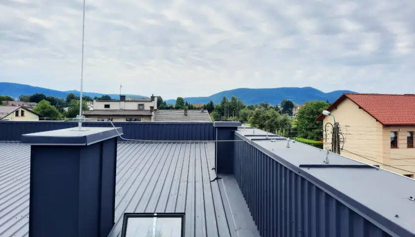 Nowoczesna instalacja odgromowa na dachu z blachy, chroniąca budynek przed burzą. Widok na góry w tle.