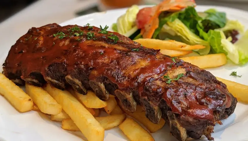 Soczyste żeberka w sosie BBQ, podane z chrupiącymi frytkami i świeżą sałatką. Prawdziwa uczta dla podniebienia!