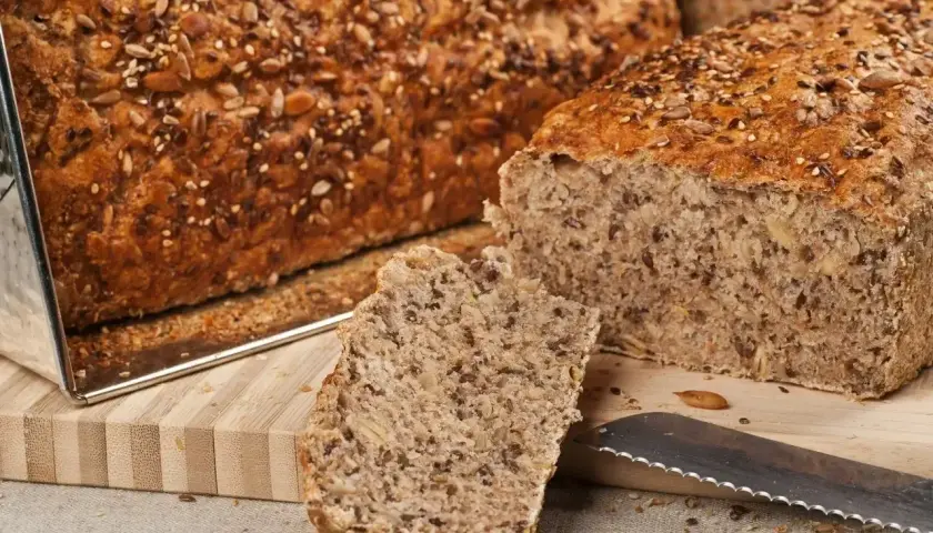 Chleb ig pełnoziarnisty, bogaty w ziarna słonecznika, lnu i sezamu, z kromką na desce i nożem.