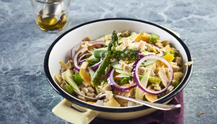 Salade de crozet colorée avec asperges, oignons rouges, pommes et dés de jambon, servie dans un plat émaillé.