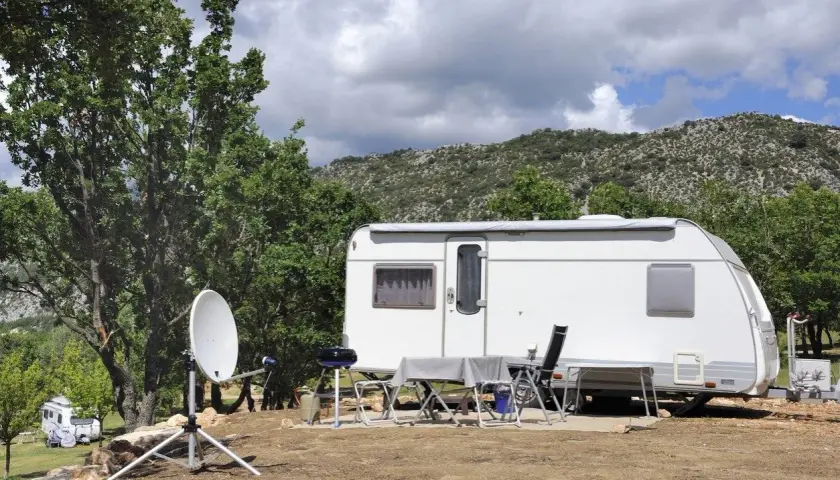 Schéma installation TV camping-car : parabole satellite devant une caravane, avec table et chaises dressées pour un repas en plein air.