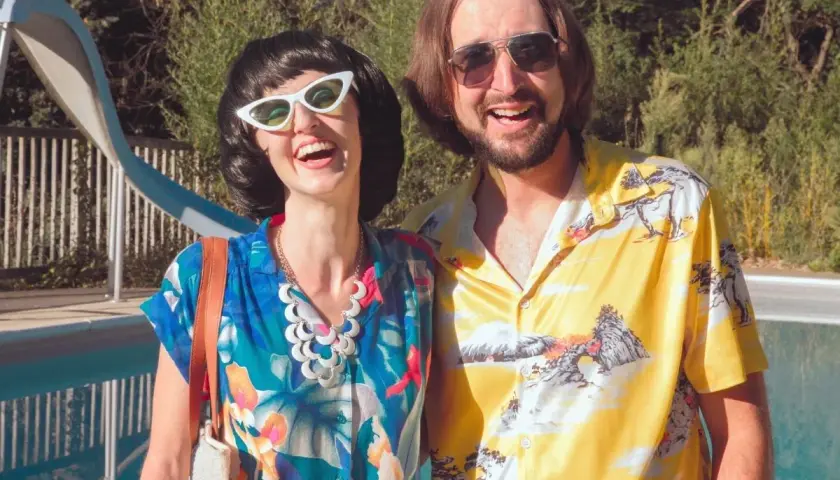 Para impreza w stylu PRL jak się ubrać? Ona w kwiecistej bluzce i białych kocich okularach, on w żółtej koszuli z motywem górskim.