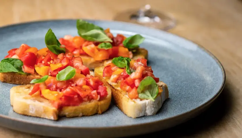 Bruschetta mit frischen Tomaten und Basilikum, ein klassisches rezept bruschetta original italienisch, auf einem grauen Teller serviert.