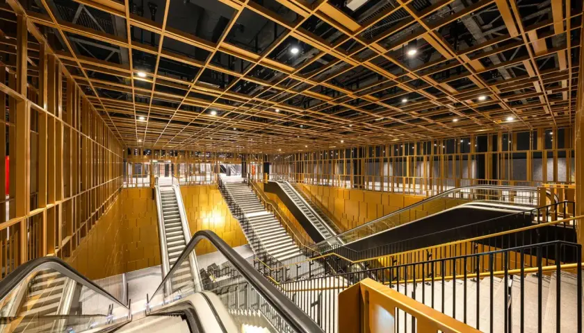 Interni moderni di una stazione metro con soffitto a griglia dorata, scale mobili e gradinate. Un assaggio delle future metro c fermate.