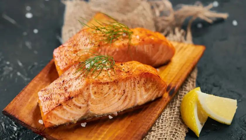 Deux pavés de saumon grillé, parsemés d'aneth et de gros sel, servis sur une planche en bois avec des quartiers de citron. Un délice pour accompagner un bon vin.