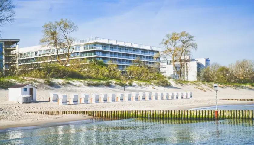 Nowoczesny seaside park hotel z widokiem na plażę i morze. Rząd białych leżaków plażowych czeka na gości.